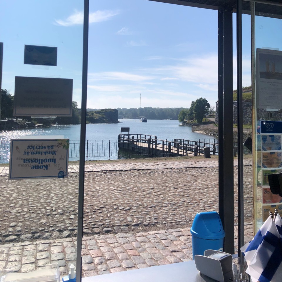 Tykistölahti ja laituri aurinkoisena kesäpäivänä kioskista kuvattuna, vesibussi saapumassa Suomenlinnaan.