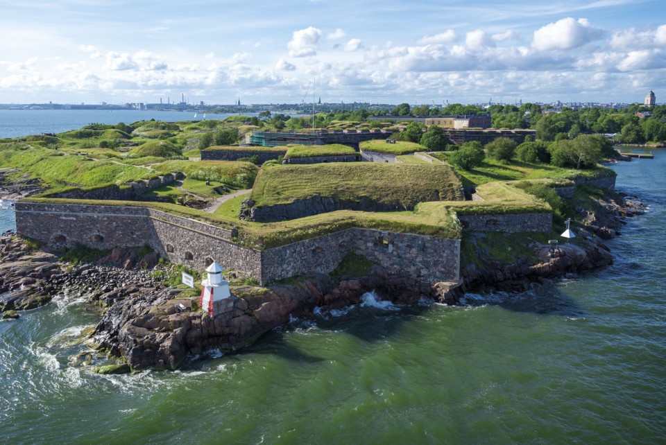 Mereltä kuvattu aurinkoinen ja vehreä Kustaanmiekka -saaren kärki, jossa bastionilinnoituksen muoto. Ylälaidassa cumuluspilviä Helsingin yllä.